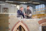 Mit Hammer und Kelle: Ausbildungsmeister Maurer erklärt Auszubildenden Mauerwerk in Osnabrück.